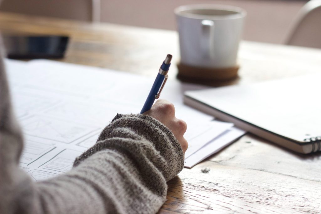 Person writing at desk with pen